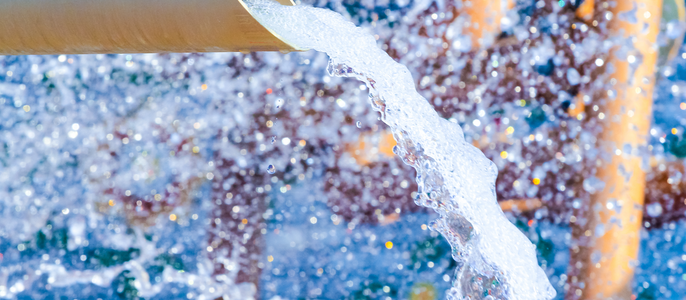 Eine Wasserleitung, aus der Wasser spritzt, vor einem Hintergrund bunter Strukturen.
