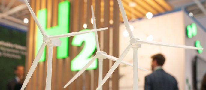 Drei Windturbinen im Vordergrund, im Hintergrund eine Holzkonstruktion und ein Neonschild mit der Aufschrift "H2".