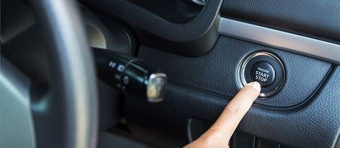 Die Hand einer Person drückt einen Knopf mit der Aufschrift "ENGINE START STOP" auf dem Armaturenbrett eines Autos.