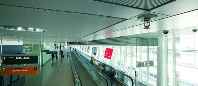 Ein moderner Flughafenkorridor mit einem Fahrsteig, Beschilderung und einer Überwachungskamera.