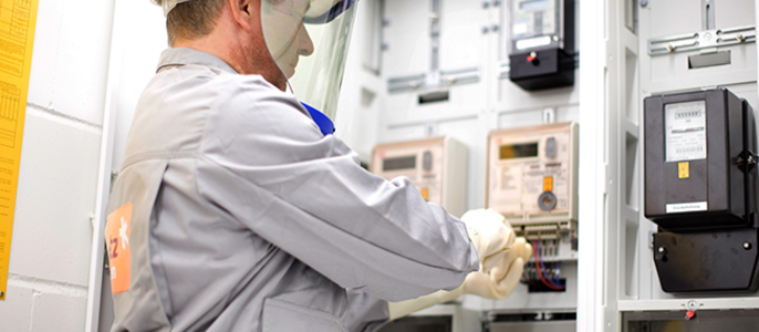 Ein Mann mit Schutzausrüstung, einschließlich Helm und Gesichtsschutz, arbeitet an einer elektrischen Schalttafel.