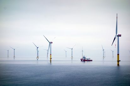 Eine weite, ruhige Wasserfläche mit mehreren Windturbinen, die sich am Horizont erheben, und einem Boot, das zwischen ihnen hindurchfährt.