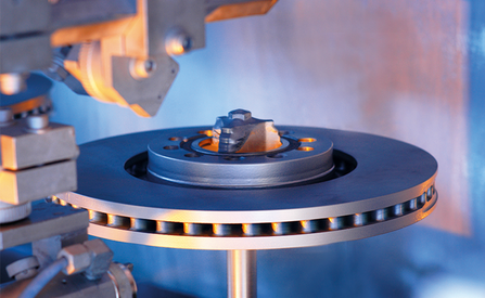 Eine Metallscheibe mit einer zentralen Nabe, die von einer Reihe von kreisförmigen Löchern umgeben ist und an einem mechanischen Arm befestigt ist.
