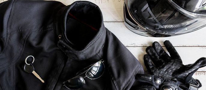 Eine schwarze Motorradjacke, ein Paar Handschuhe, ein Helm, eine Sonnenbrille und ein Schlüssel.