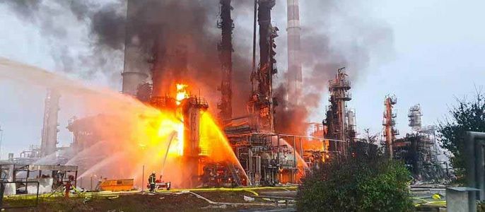 Eine große Industrieanlage steht in Flammen und hat dichten Rauch, während die Feuerwehr versucht, den Brand unter Kontrolle zu bringen.