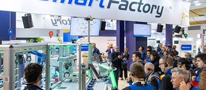 Eine Gruppe von Menschen an einem Stand mit der Aufschrift "smartFactory", wo sie eine Vorführung einer Maschine beobachten.