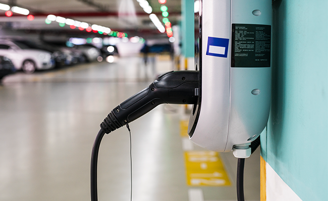 Eine Ladestation für Elektrofahrzeuge, die an einer Wand in einem Parkhaus montiert ist, mit mehreren geparkten Autos im Hintergrund.